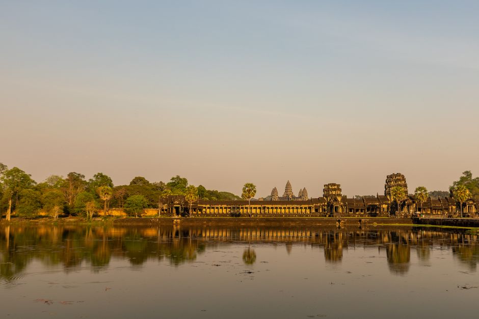 Majestic Angkor Wat temple reflecting in calm waters at sunrise, showcasing ancient architecture.